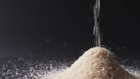 Video-of-close-up-of-sand-grains-pouring-into-heap-and-copy-space-on-black-background