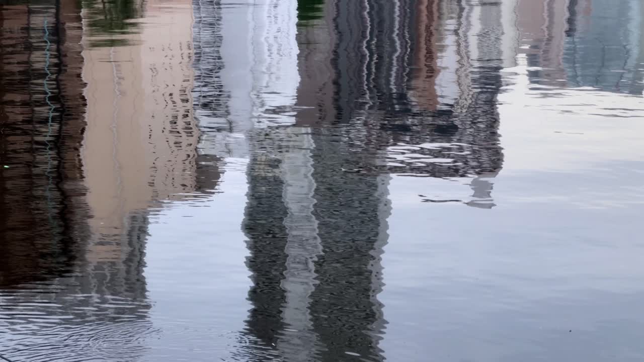 Edifici riflessi in acqua calma che creano un'immagine ondulata e astratta con un'atmosfera serena.