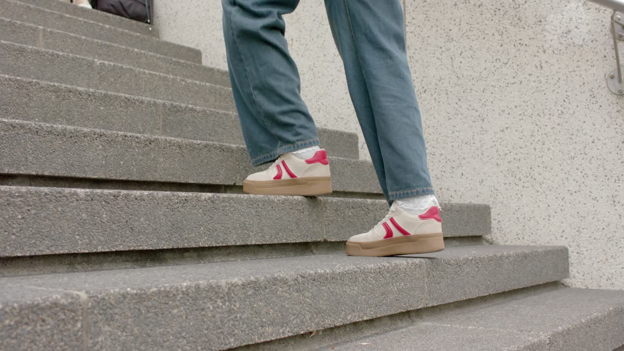 Una persona con scarpe rosse sale il primo gradino di una scala, dirigendosi verso una persona con una tazza di caffè e uno zaino.