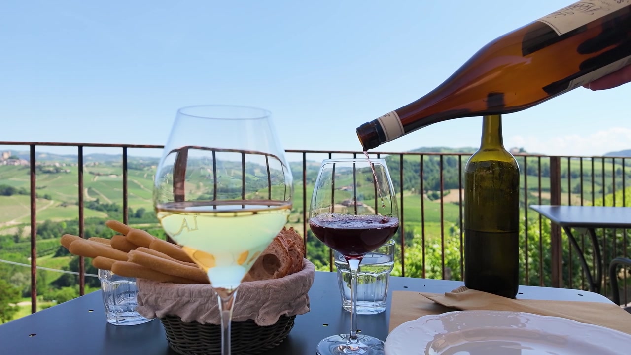 Vino rosso si versa in un bicchiere su un balcone con vista su dolci colline e vigneti rigogliosi.