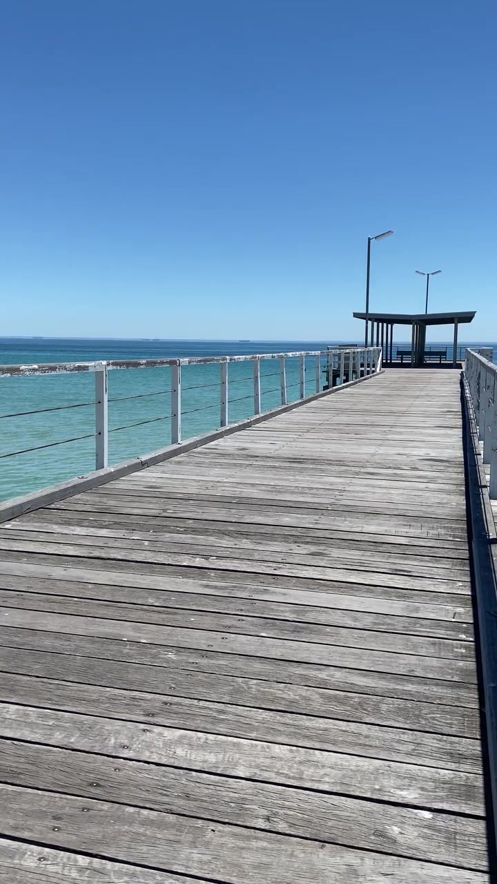 Punto de vista de video vertical caminando por un muelle de madera sobre el tranquilo mar turquesa. Un día soleado y brillante con un cielo azul despejado