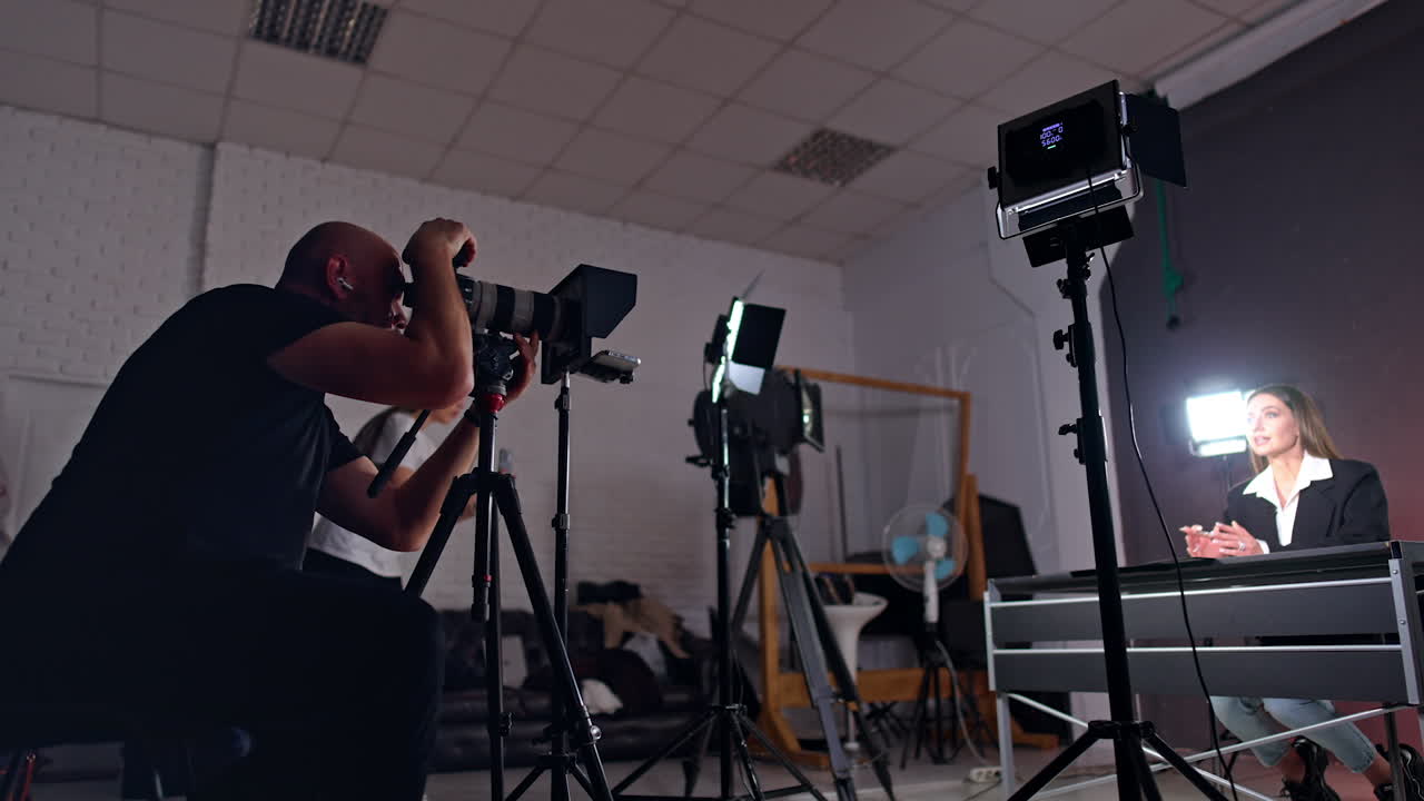 Concentrated Caucasian cameraman sits looking at his camera object lens. Brunette female talks to camera recording video for blog.