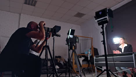 concentrated caucasian cameraman sits looking at his camera object lens. brunette female talks to camera recording video for blog.