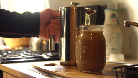 man pours coffee out of a french press into a mason jar inside an airstream