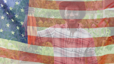 animation of flag of united states of america over happy african american farmer keeping carrots