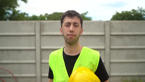 a construction worker, holding his yellow hard hat, removes his standard safety spectacles - medium close up