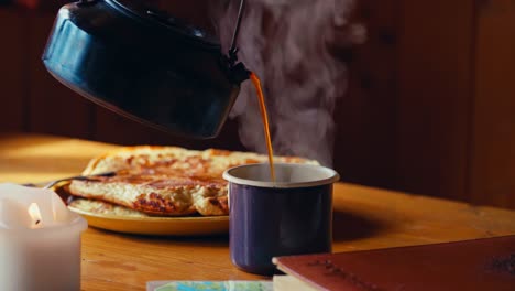 hot tea pours into a cup beside pancakes and a candle on a wooden table in reinsjøen, åfjord, trøndelag, norway - close up
