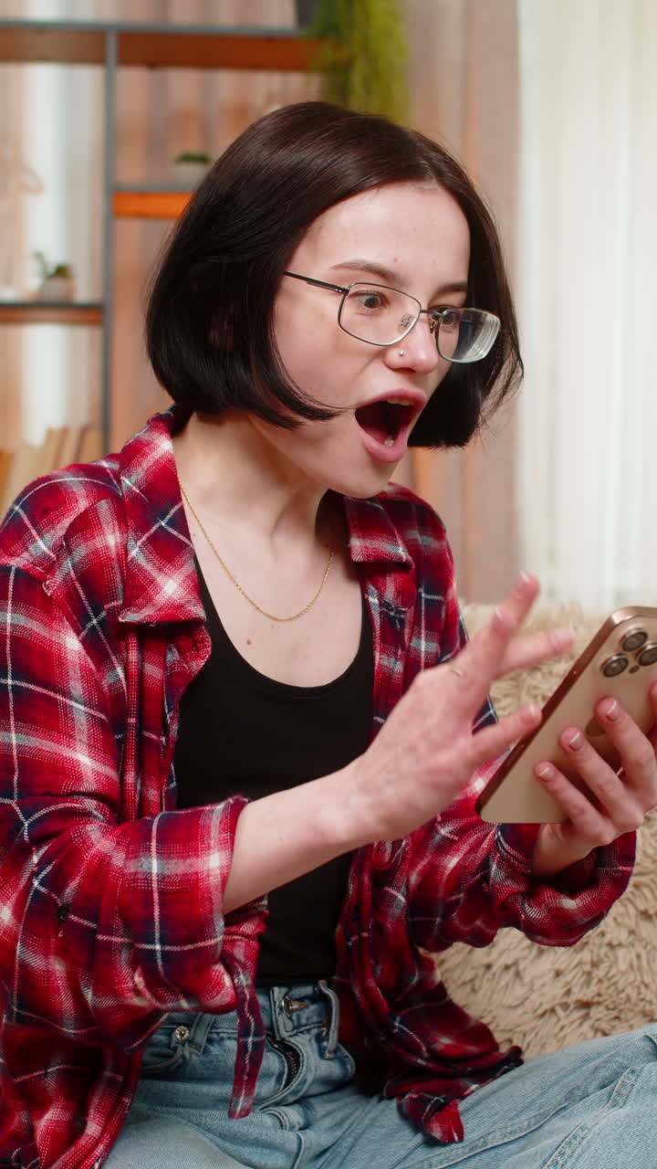 Young smiling woman using smartphone at home winning online lottery game celebrating jackpot victory