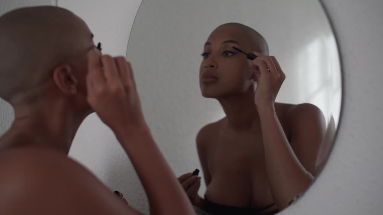 mujer negra seria aplicando rímel en las pestañas