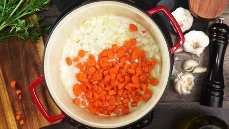 cooking orange diced carrots and diced yellow onions in a red stock pot. sizzling fresh vegetables while cooking italian wedding soup. using a wooden spoon to mix carrots and onions while they sautee.
