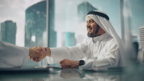 emirati empresario sonriente en blanco kandura tradicional sentado en la oficina con socios de negocios. estrechar la mano en la inversión exitosa. saudí, emirati, concepto de empresario árabe.