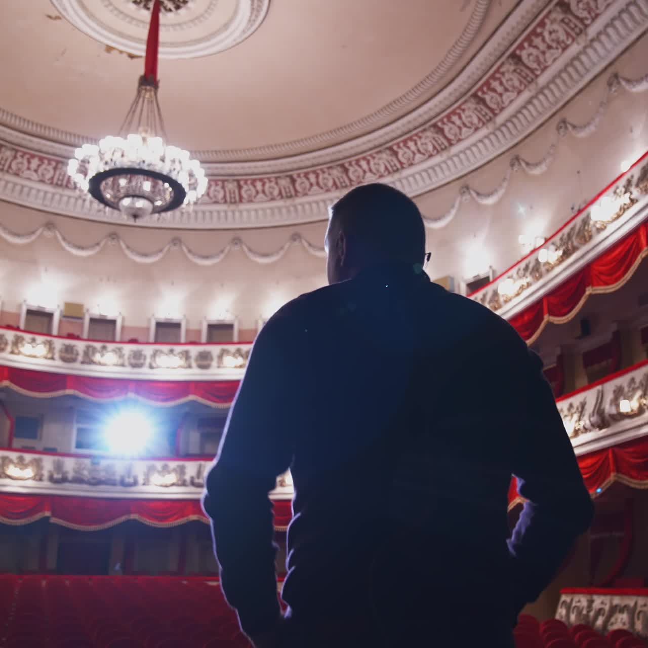 Man talking on a scene of a large theatre. Actor practising on stage before the performance in empty auditorium. Back view.