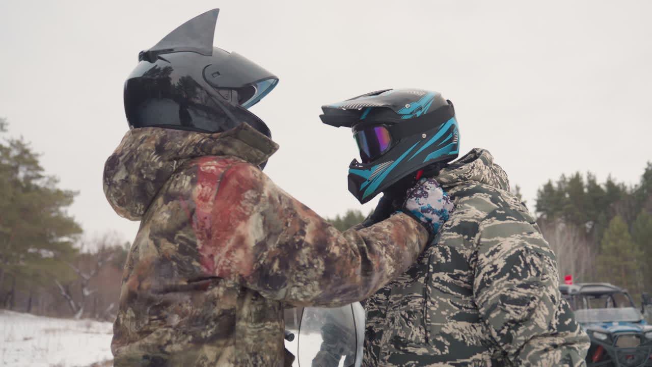 White riders adjusting helmets snowy forest, guide secures strap and visor with steady hands, camo jackets and goggles reflecting pine trees, snowmobile nearby, cold overcast light, teamwork