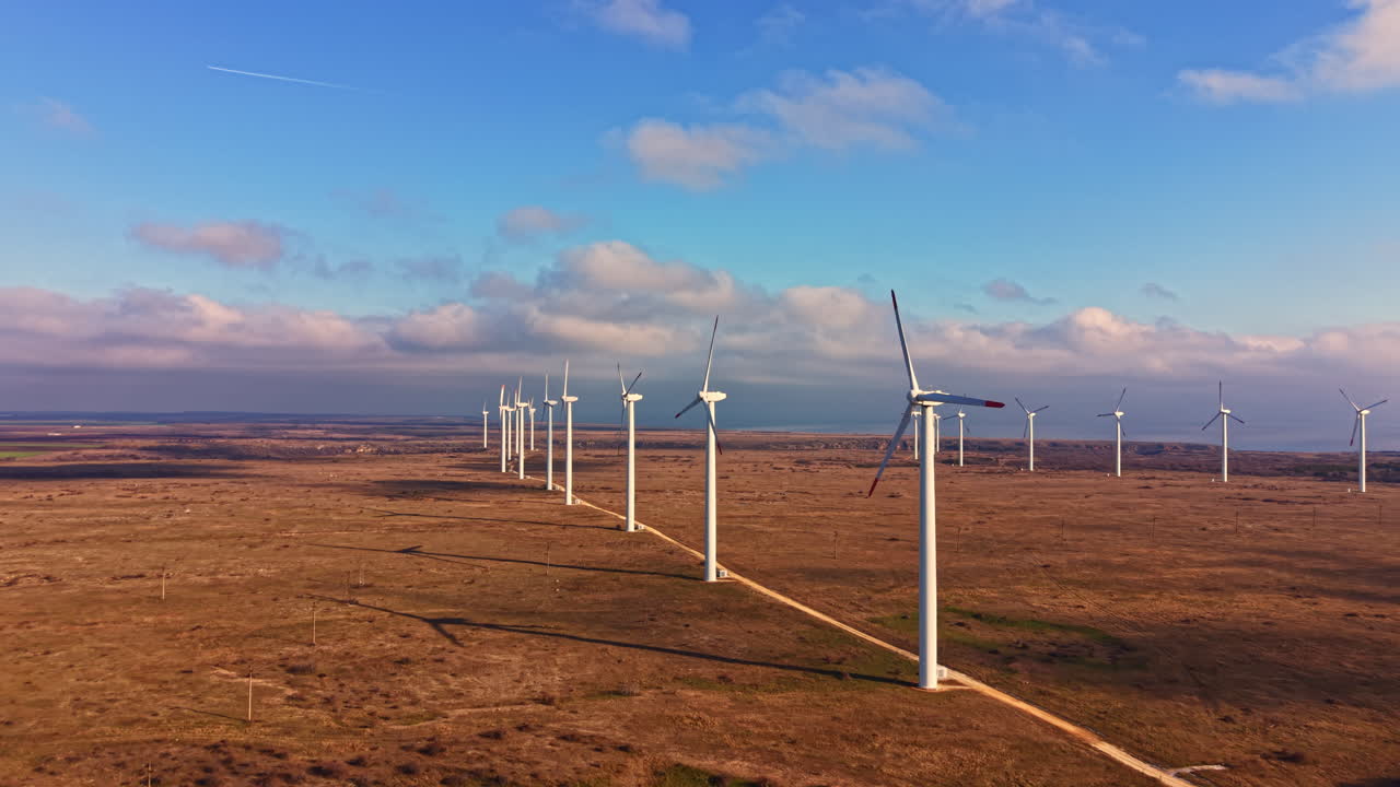 Turbinas eólicas enfileiradas em uma paisagem plana sob um céu parcialmente nublado na luz da tarde, criando energia renovável