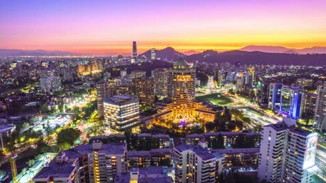 Aerial-hyperlapse-establishing-in-Santiago-Chile,-modern-architecture-with-island-hills-with-sunset-in-the-background,-city-lights-at-night