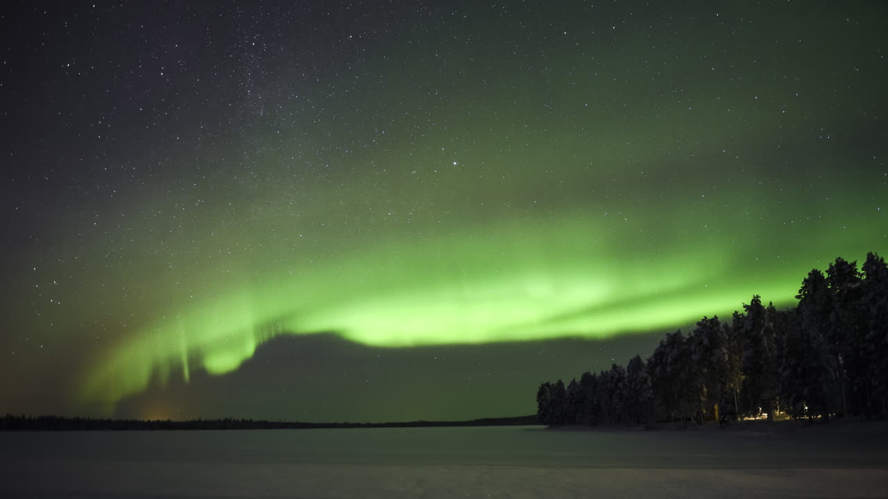 Northern lights timelapse of bright green aurora borealis in the night sky, with stars. Time lapse over remote landscape of frozen lake and forest in Lapland, Finland