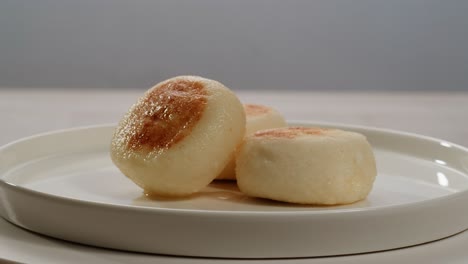 un primer plano detallado de tres panes cocidos al vapor de color marrón dorado artísticamente colocados en un plato blanco prístino, listos para ser disfrutados