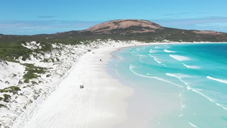 excellent aerial shot of cars driving on the white sands of wharton bay as clear blue water laps the shore in esperance, australia