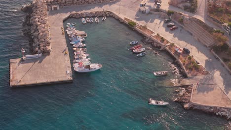 Aerial-high-angle-overview-of-small-port-in-Donousa-Greece-with-sparkling-green-blue-ocean-water-at-sunset