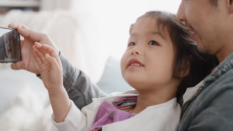 Padre-Asiático-Y-Niño-Usando-Un-Teléfono-Inteligente-Teniendo-Video-Chat-Niña-Saludando-Compartiendo-El-Fin-De-Semana-Con-Papá-Disfrutando-Charlando-Por-Teléfono-Móvil-Con-Un-Amigo-4k