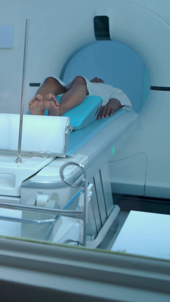 Video verticale: Inizio scansione, tavolo mobile che trasporta un uomo in pantaloncini con cuneo nella risonanza magnetica nella sala di scansione