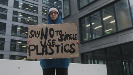 young female climate activist with banner protesting against the single use plastics while looking at camera