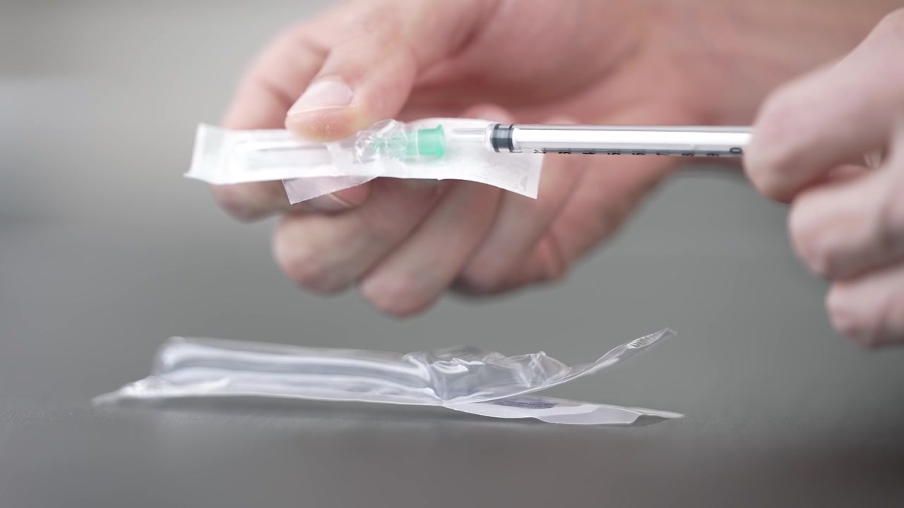 Hands open a sterile syringe package and attach a needle onto it