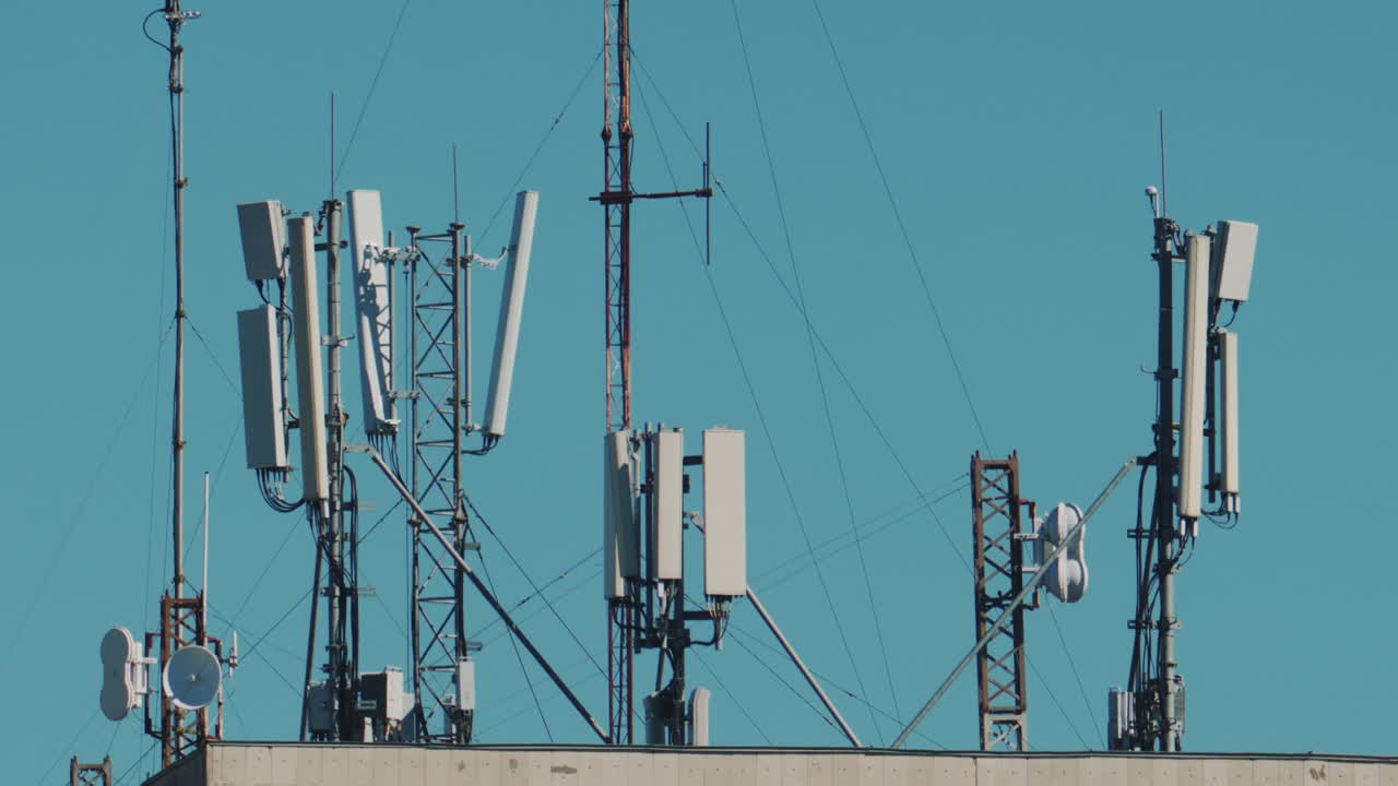 Telecommunication antennas and towers installed on a rooftop against a clear blue sky
