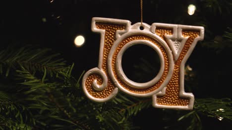 a hand-painted christmas ornament saying "joy" hanging on a christmas tree