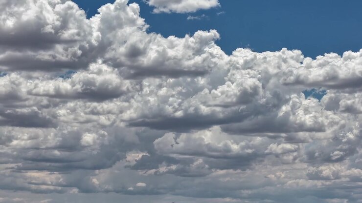 4K drone timelapse capturing beautiful layers of fluffy, textured cumulus clouds shifting dynamically against a bright blue sky. Sunlight highlights the dense, rolling cloudscape on a clear afternoon.