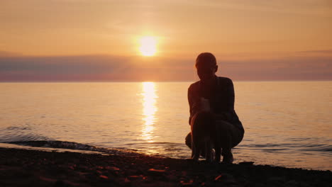 Frau-Spielt-Mit-Einem-Hund-Am-See-Bei-Sonnenuntergang