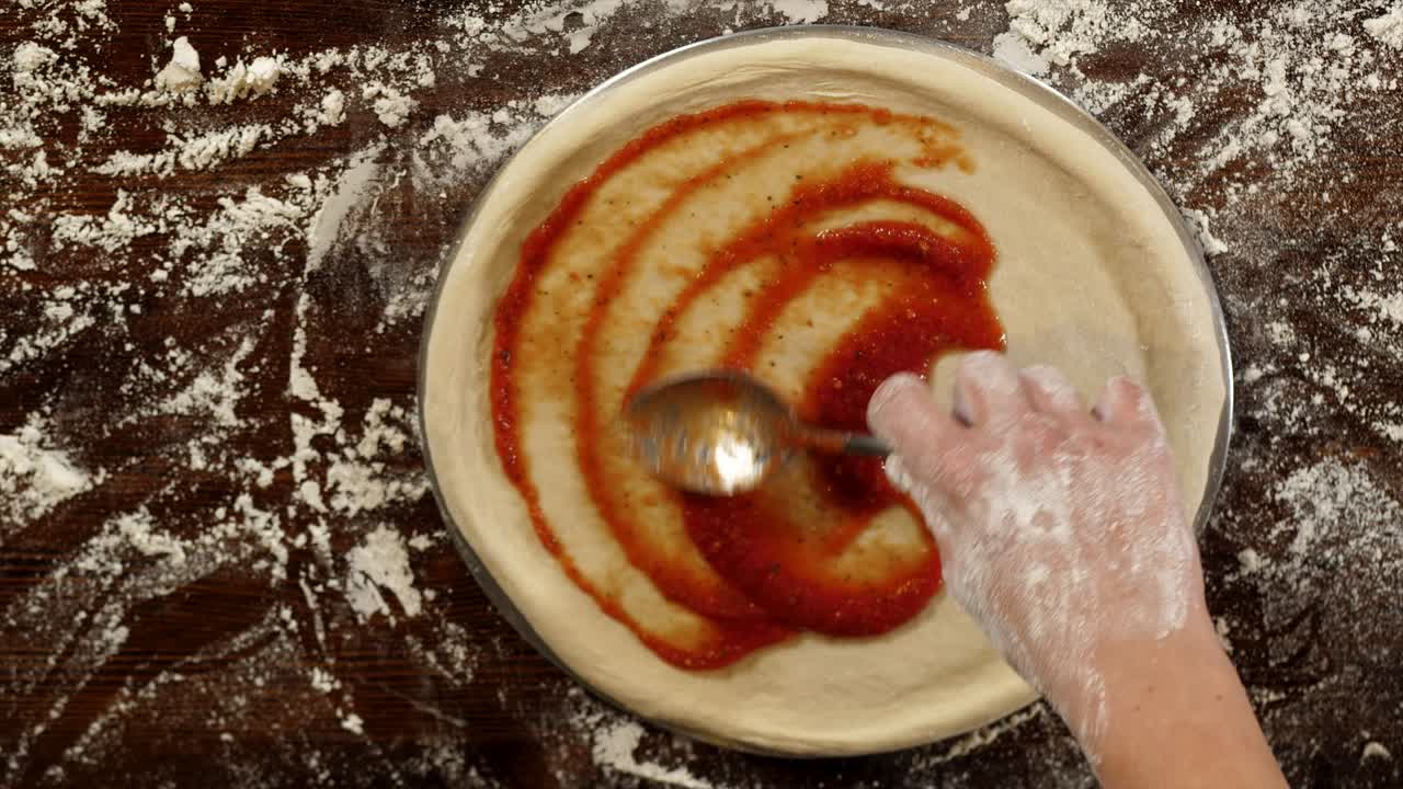 Primo piano della stesura della salsa di pomodoro sull'impasto della pizza