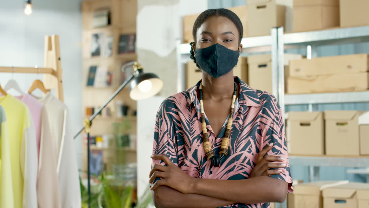 African American woman designer in black mask looking at camera in positive mood in clothing store