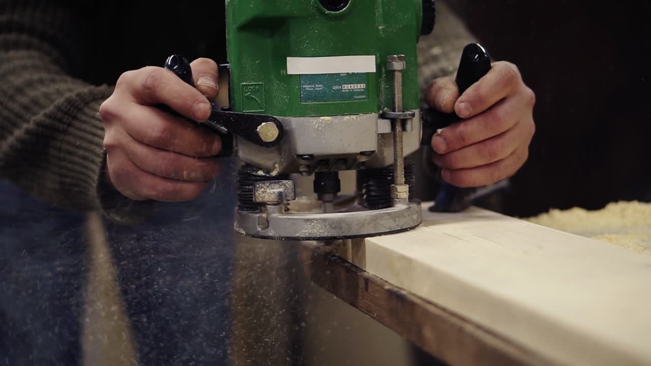 muy de cerca de un artesano manos trabajando con el pulido con la máquina de rectificado manual en el taller de madera. muele una gran tabla de madera. polvo y astillas se dispersan en el suelo. persona irreconocible. cámara lenta