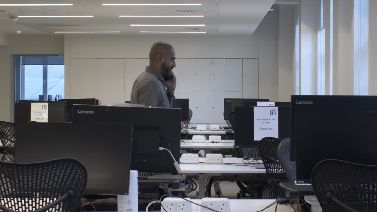 Adult Male Talking On Phone Walking Back And Forth In Between Empty Desks. Locked Off