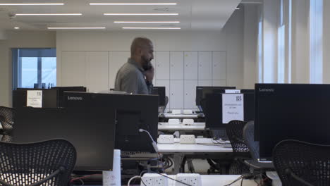 adult male talking on phone walking back and forth in between empty desks. locked off