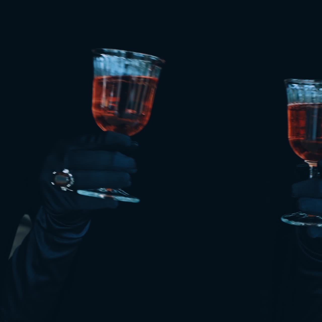 Wine in glass in hands on black background. Charming female hands in black gloves holding two glasses with red drink. Enigmatic atmosphere.