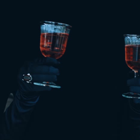 wine in glass in hands on black background. charming female hands in black gloves holding two glasses with red drink. enigmatic atmosphere.