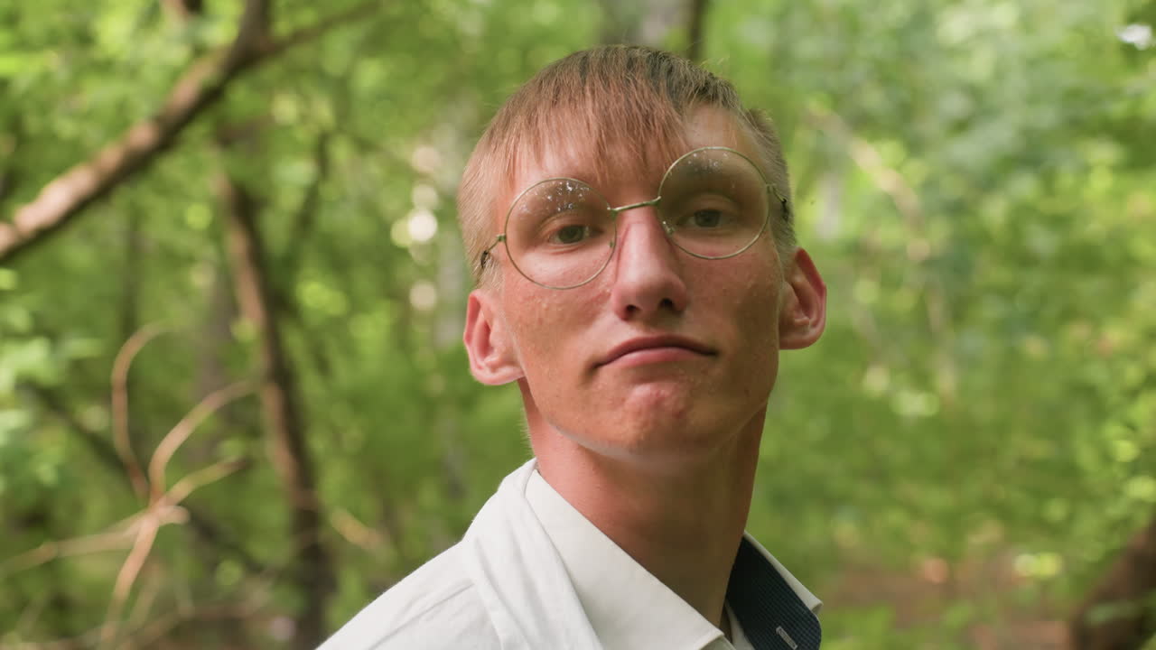 Man standing in forest adjusting white coat while looking focused, surrounded by lush greenery and soft natural light, highlighting outdoor preparation, concentration, and lifestyle detail