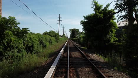 A-low-angle-view-looking-straight-down-train-tracks-with-green-trees-on-either-side