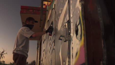 young male street artist graffiti spray painting text on abandoned building wall