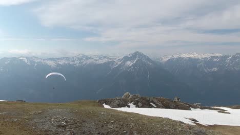 Aerial-drone-tracking-shot-of-Paraglider-flying-between-snowy-mountains-during-sunlight---Spectacular-extreme-sport-footage