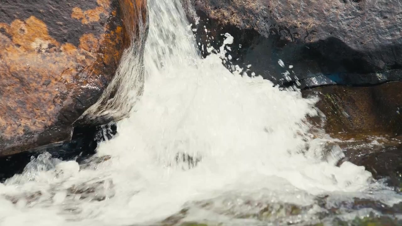 Acercamiento lento a una pequeña cascada de montaña que se precipita entre rocas erosionadas, capturando agua dulce prístina, movimiento y la naturaleza alpina. Filmado en cámara lenta. Pequeño movimiento.
