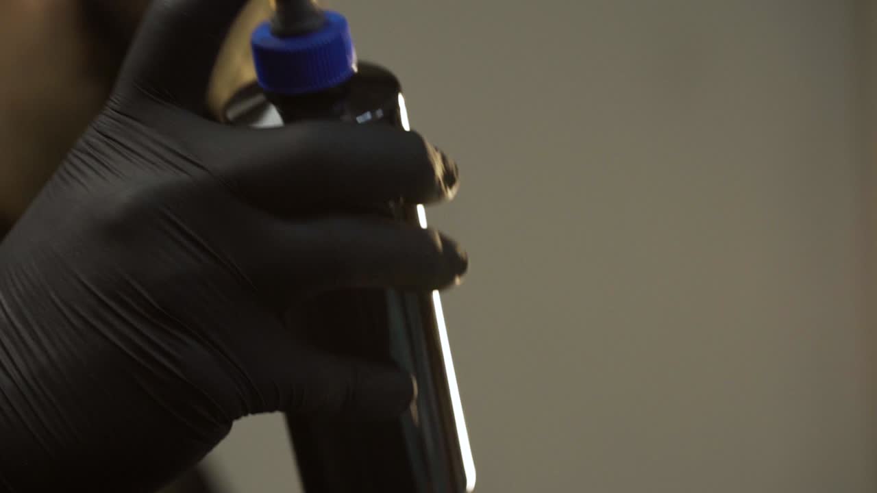 Tattoo artist with black gloves shaking bottle of black ink during preparation, shot in slowmotion 120fps