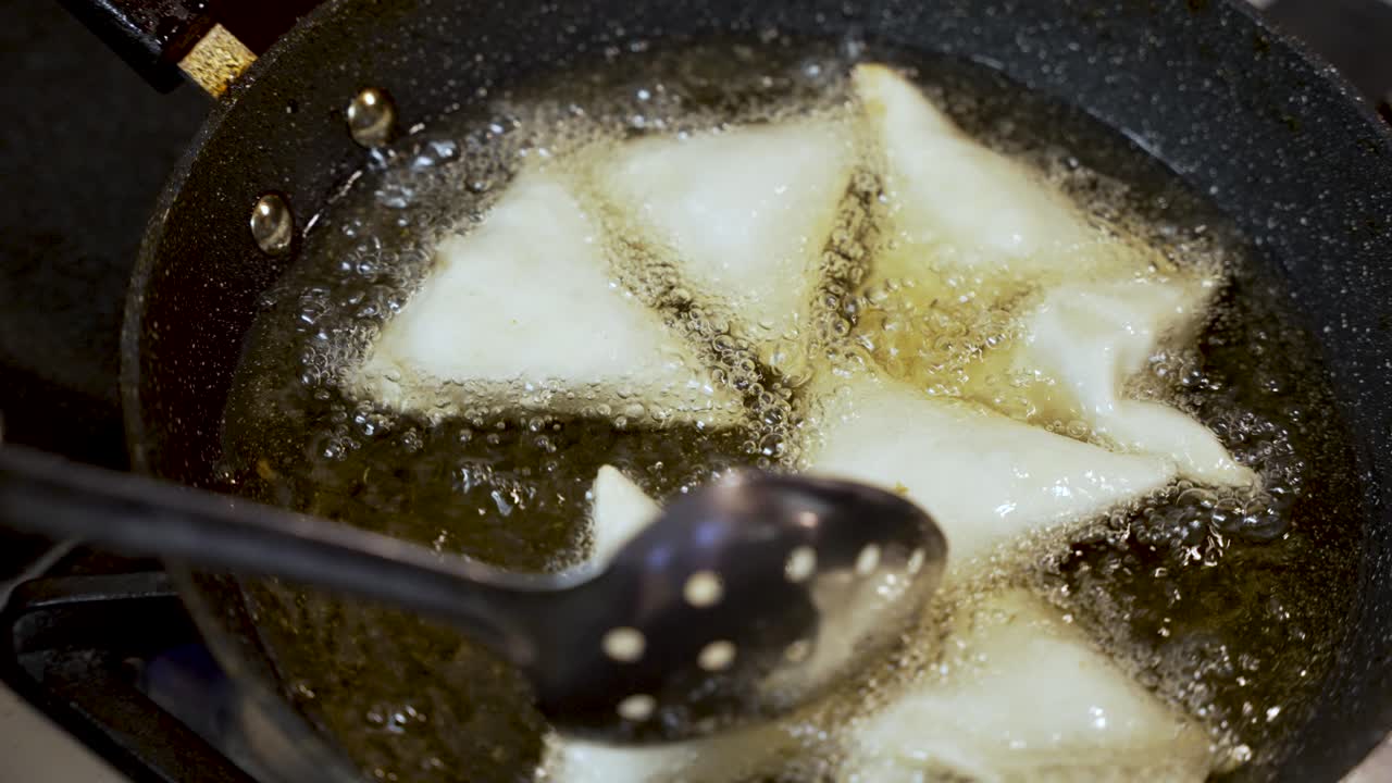 Chef frying crispy samosas in hot oil, using a slotted spoon to ensure even cooking in a bubbling pan, creating a delicious snack