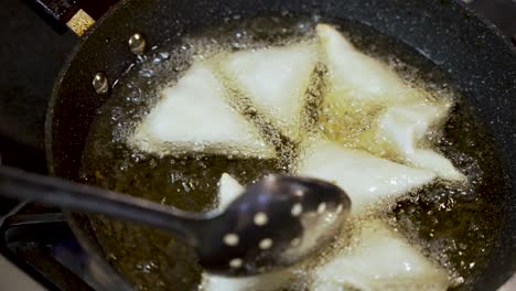 chef frying crispy samosas in hot oil, using a slotted spoon to ensure even cooking in a bubbling pan, creating a delicious snack
