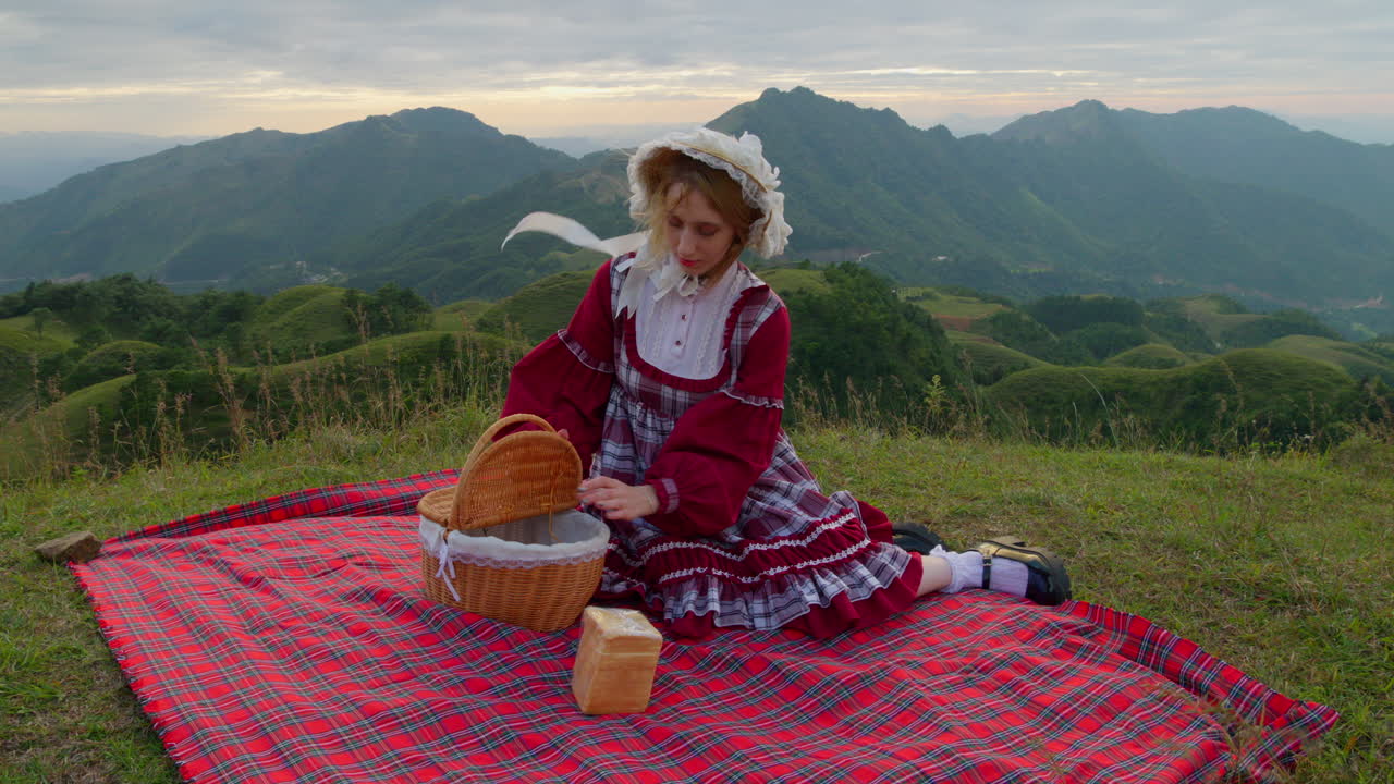 hermosa joven con ropa tradicional europea traje renacentista sentada en la hierba almorzando con pintorescas montañas paisaje en el fondo