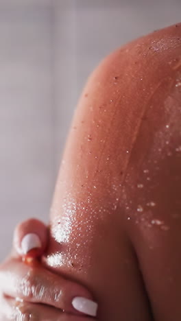 woman cleans skin with scrub in shower unit closeup. lady uses natural cosmetic product to exfoliate dry skin in bathroom. beauty routine at home