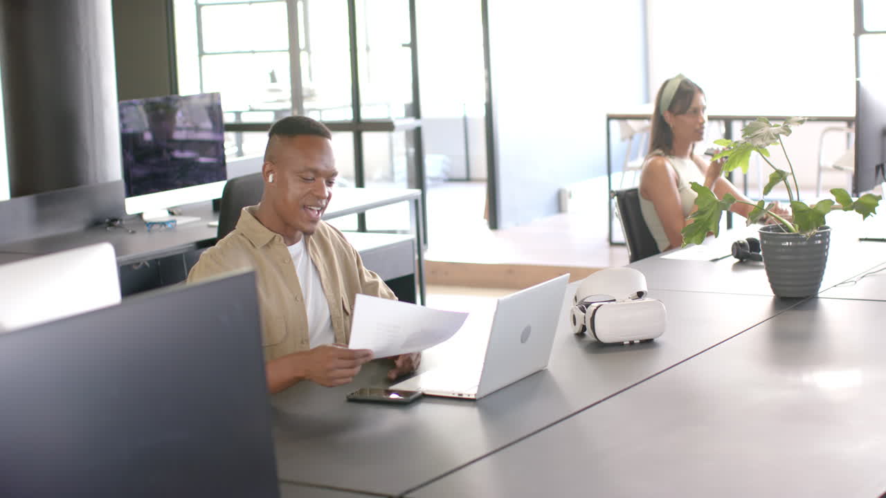 Smiling man reviewing documents at desk with laptop and smartphone in office
