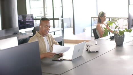 smiling man reviewing documents at desk with laptop and smartphone in office